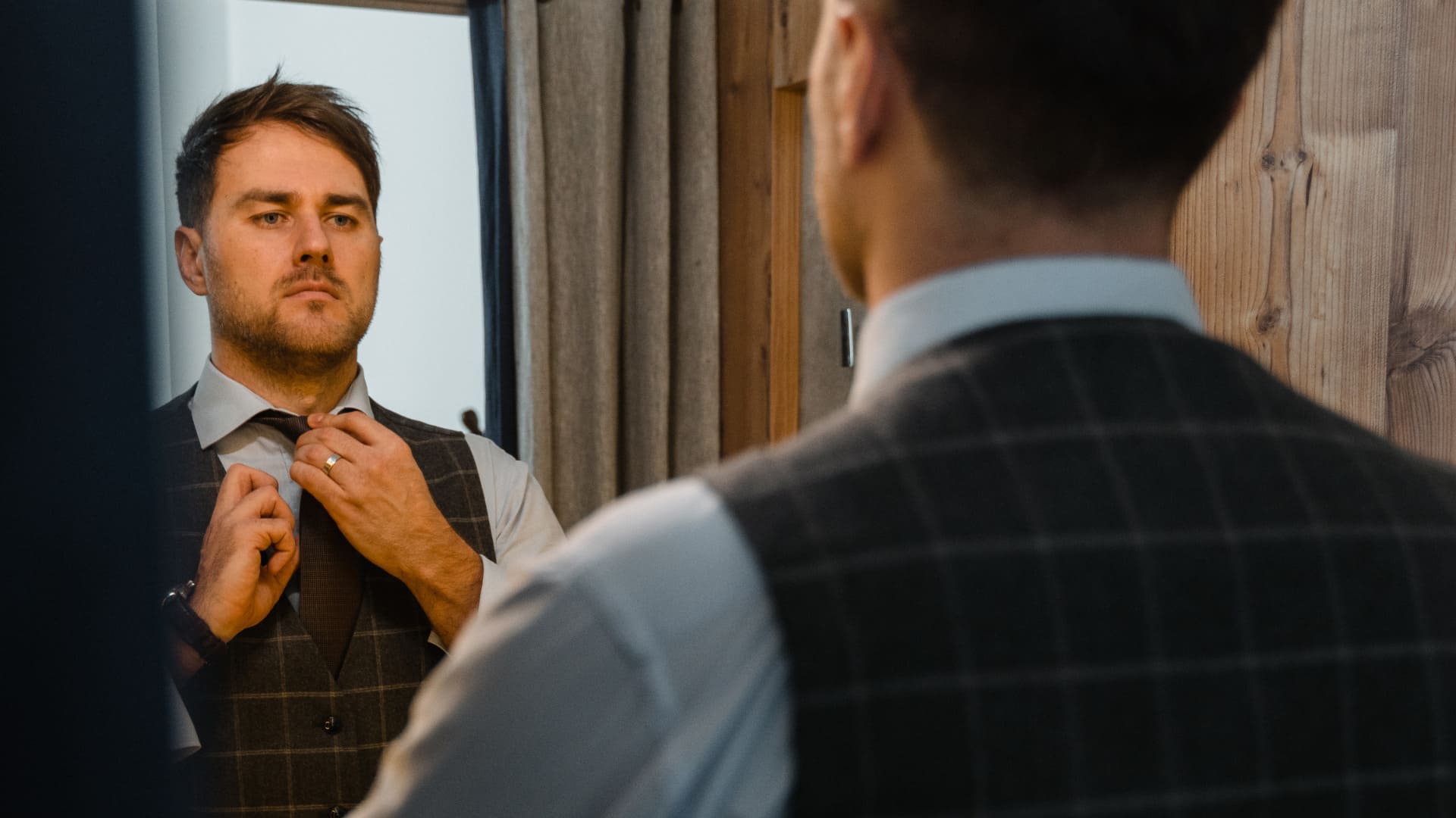 Homme devant un miroir en train de refaire son nœud de cravate